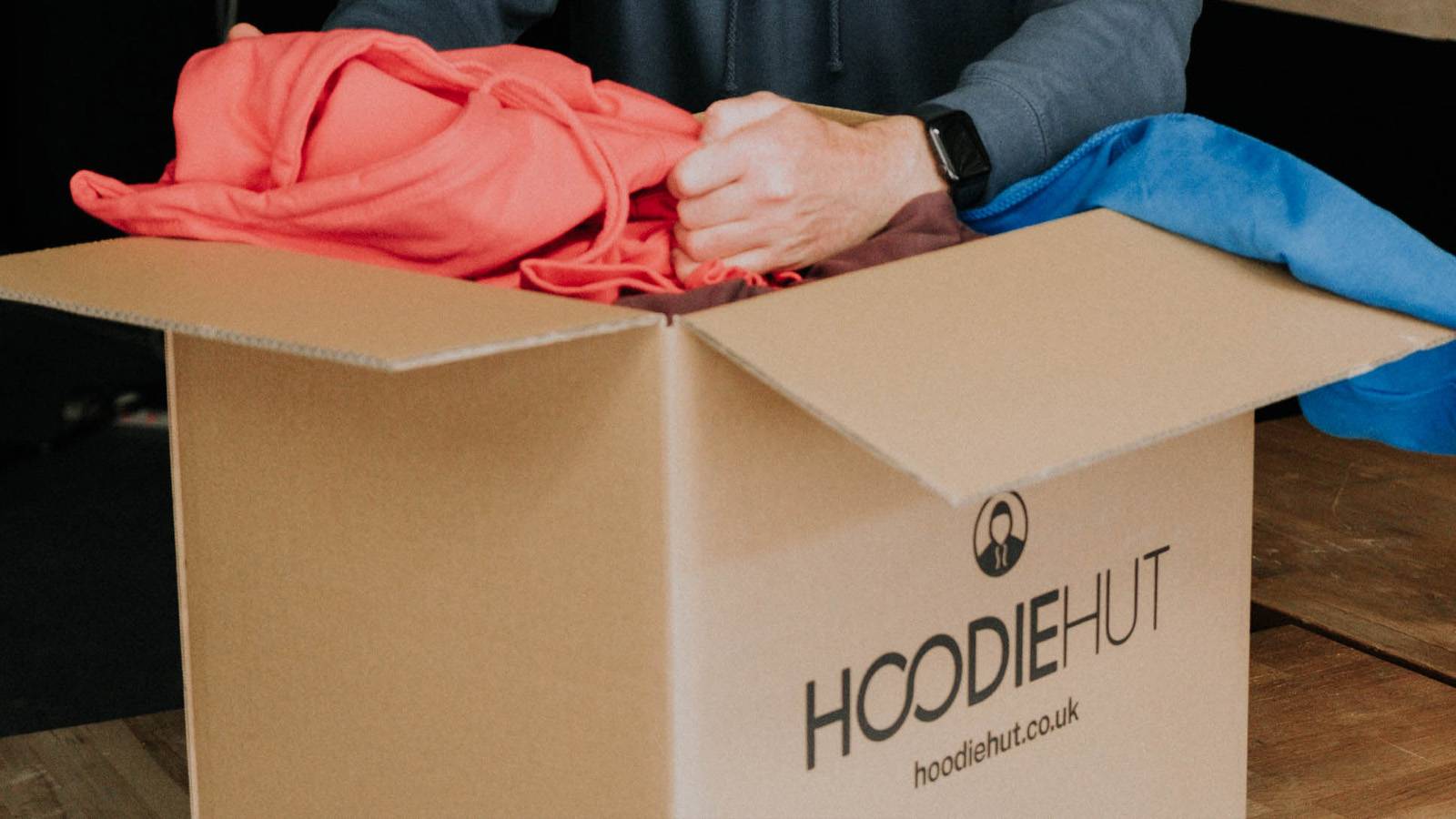 a person pulling a leavers hoodie out of a box with HoodieHut branding on the side